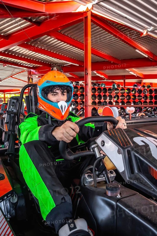 Young man wearing a racing suit and helmet, focusing on driving a go kart, preparing for a race at an indoor karting facility, enjoying the motorsport experience