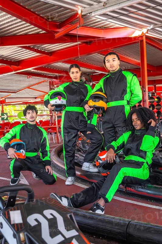 Diverse group of young people wearing racing suits and holding helmets, preparing for a fun karting competition, embodying teamwork and leisure at an indoor track