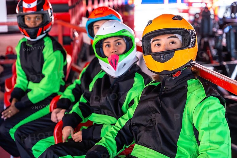 Young diverse friends in helmets and racing suits sit in go karts on an indoor track, ready and focused for a fast, fun, adrenaline filled karting race together