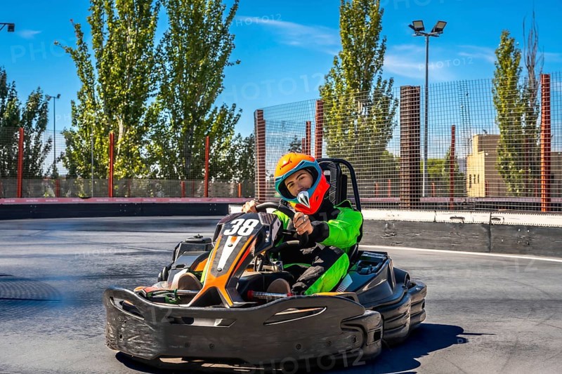 Young man in helmet and racing suit zooming a go kart on an outdoor asphalt track, enjoying speed and competition on a sunny day during a weekend karting session