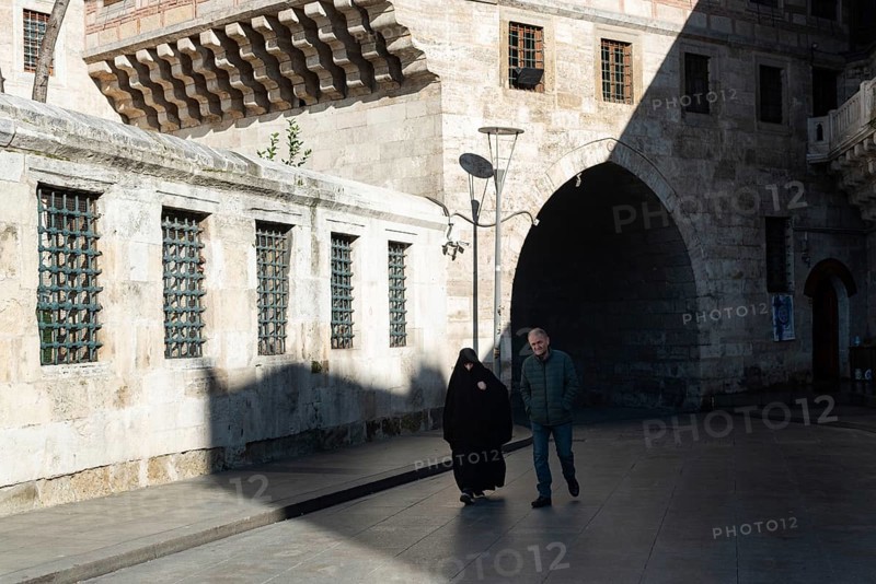 Istanbul, Turkey. January 3rd 2025. A Muslim couple walk behind Yeni Camii or New Mosque in the Fatih district of the European side of Istanbul, Turkey