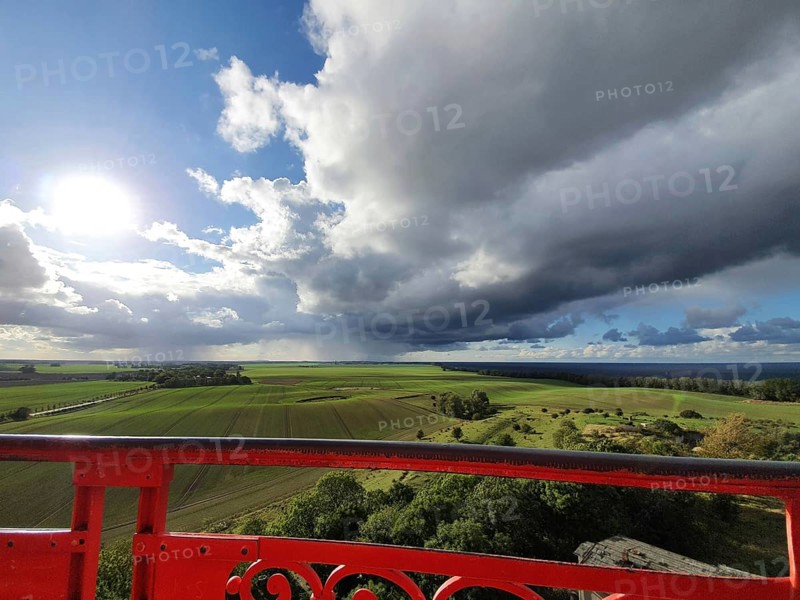 View of green fields under dramatic sky with dark clouds, red railings in the foreground and sunshine, Cape Arkona lighthouse, Rügen