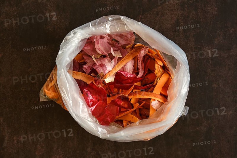 A clear plastic bag holds various vegetable peels and scraps. The bag sits on a dark countertop, showing the colorful waste from food preparation in a kitchen