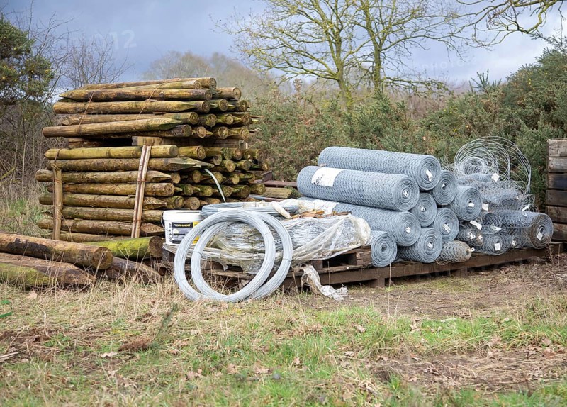 Agricultural fencing supplies wooden fence posts, rolls of wire stacked outdoors post-and-wire fencing system, UK