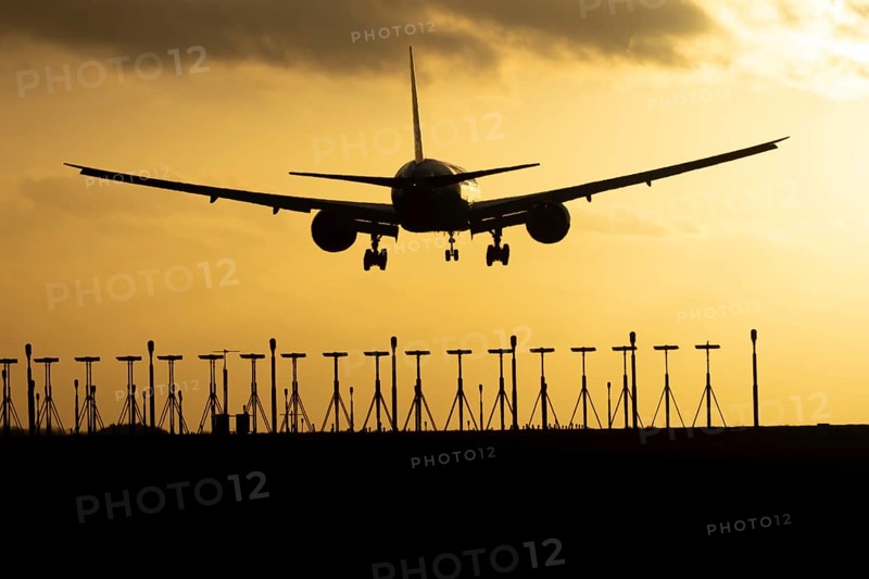 Boeing 777 commercial passenger jet aircraft in flight on approach to land over runway lights silhouette at sunset at London Stansted airport, Essex, England, United Kingdom