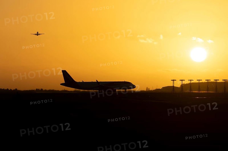 Airbus commercial passenger airliner jet aircraft taking off in flight with another plane on the taxiway at sunset at London Stansted airport, Essex, England, United Kingdom