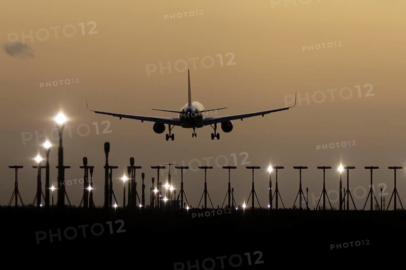 Airbus 320 commercial passenger airliner jet aircraft in flight on approach to land over runway lights at sunset at London Stansted airport, Essex, England, United Kingdom