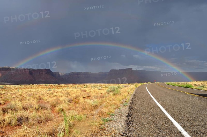 Another rainbow over a long, empty road in a colorful desert landscape with cloudy sky, Canyonlands National Park, Utah, USA