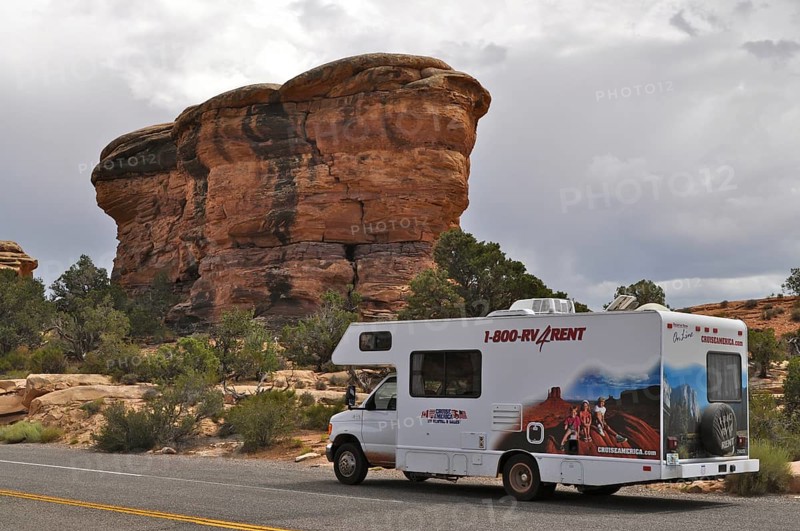 Motorhome standing on a road in front of a distinctive rock formation under a cloudy sky, Canyonlands National Park, Utah, USA