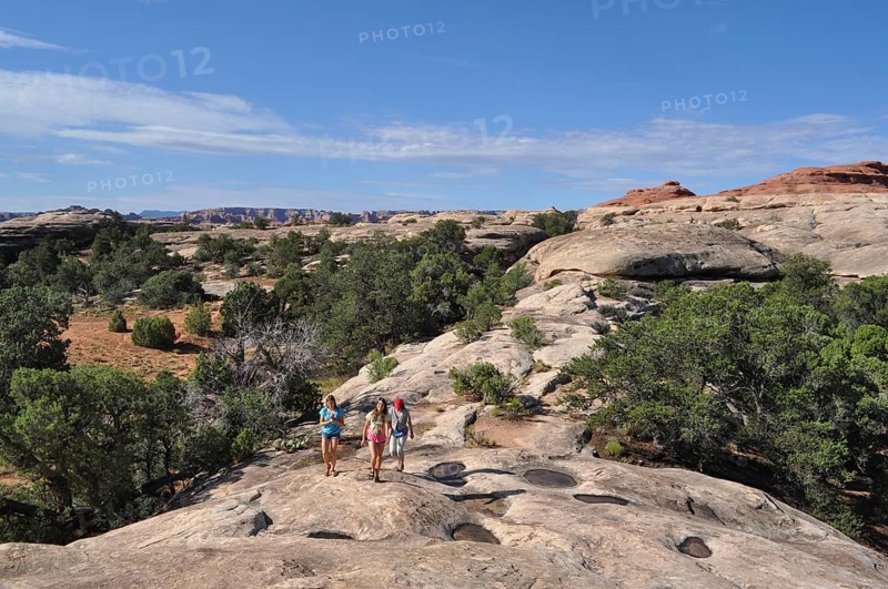 A family wandering across rocky terrain in a desert landscape under blue skies, Canyonlands National Park, Utah, USA