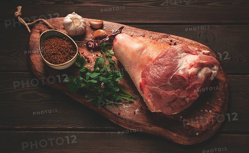 Raw pork knuckle, on a wooden chopping board, with spices, close-up, top view, no people