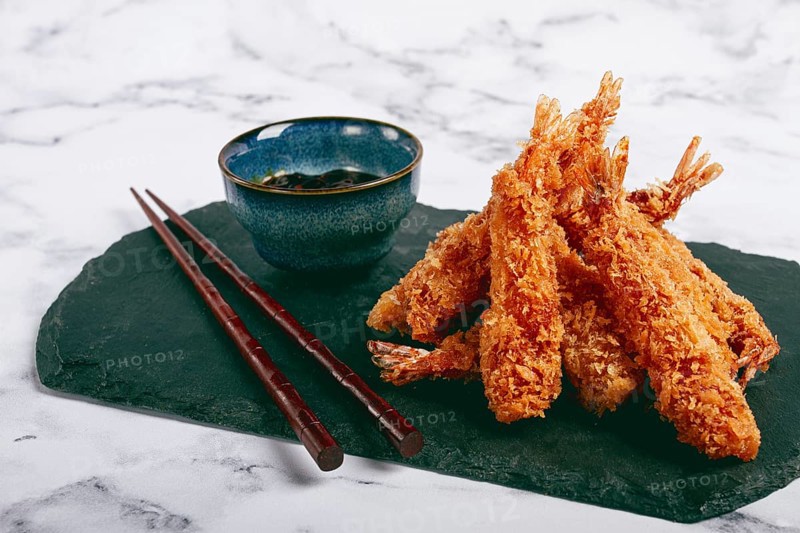 Shrimp in tempura, deep fried, on black slate, with sauce, light marble table, no people