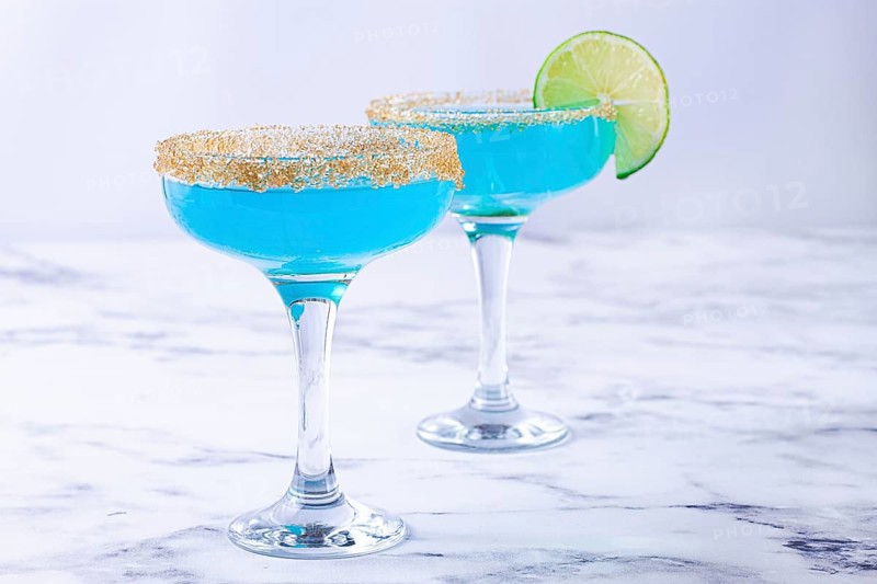 Colorful blue cocktails in elegant glasses with lime garnish on a marble table