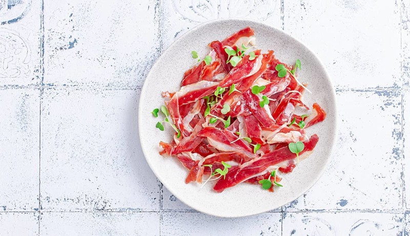Ham of duck breast, dried duck fillet, with microgreens, plate, on a tiled table