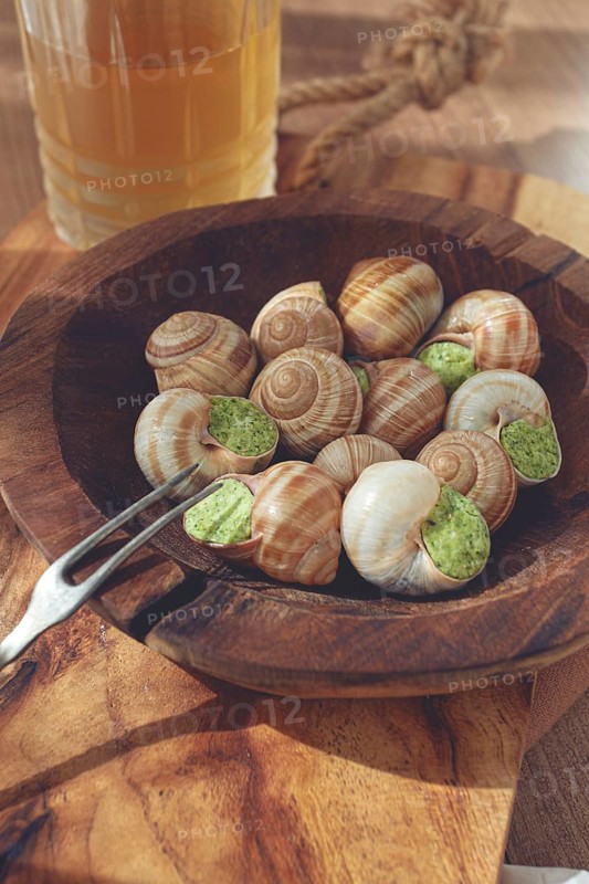 Snails cooked with herb oil on a wooden plate, served with white wine, natural light, no people