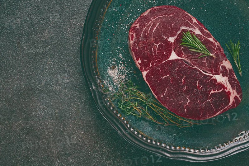 Steak made from fresh beef, with herbs and various spices, on a plate, ready to cook, there are no people