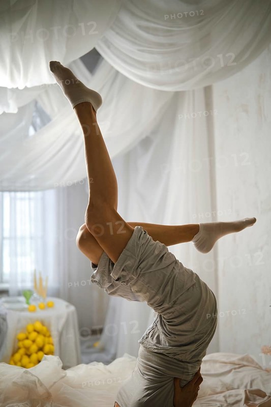 A person is upside down in a yoga pose in a bright room. The space is filled with white drapes and has a table with lemons. Sunlight comes through the windows, creating a warm atmosphere