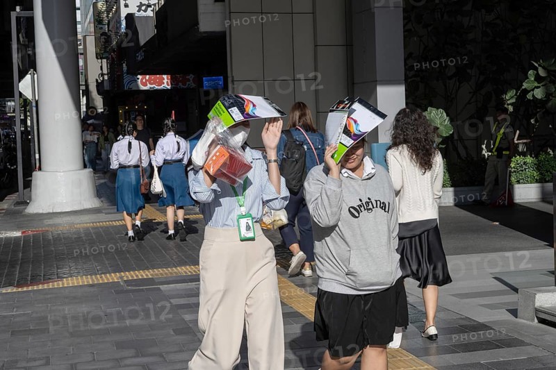 Bangkok, Thailand. March 25th 2025. People shield their faces from the bright sun and wear face masks during the intense summer heat in the Thai capital, Bangkok, Thailand