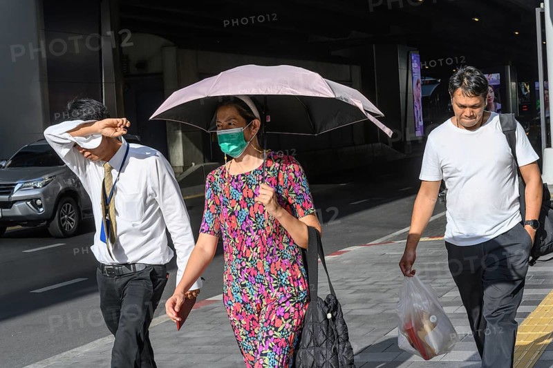 Bangkok, Thailand. March 25th 2025. People shield their faces from the bright sun and wear face masks during the intense summer heat and harsh climate in the Thai capital, Bangkok, Thailand