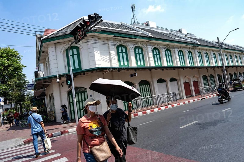 Bangkok, Thailand. March 25th 2025. People crossing the street with masks and an umbrella due to poor air quality and excessive summer heat near Wat Mangkon metro station, Bangkok, Thailand