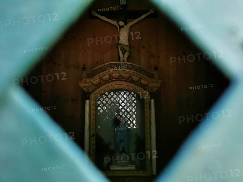 Wooden statue of Jesus on the cross through a grid in a dark chapel, hiking in the Frankenwald nature park Park, Upper Franconia