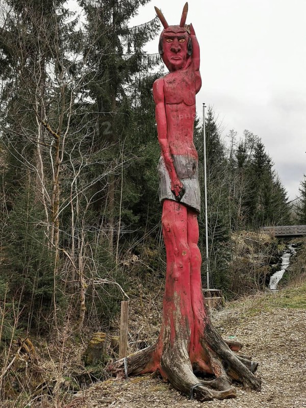 A red wooden sculpture at the entrance to Höllental in the shape of a devil looms in the forest, Frankenwald nature park Park