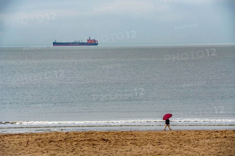 Winter break, on Zeedijk-Knokke, beach promenade in Knokke-Heist, beach walkers with umbrella when it rains, dreary winter day, freighter on the North Sea, Belgium