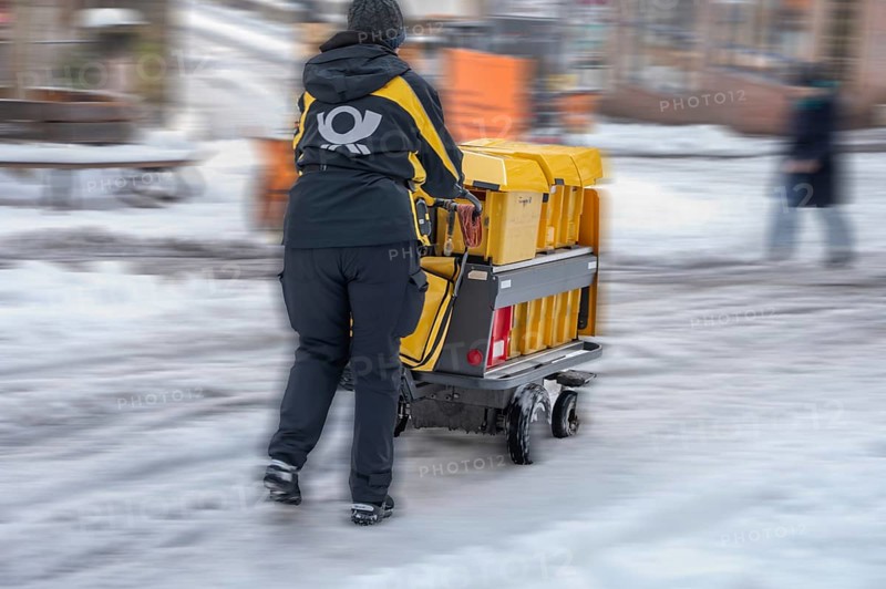 Movement, postman walking with loaded handcart on a wintry road in the city, Nuremberg, Middle Franconia, Bavaria, Germany