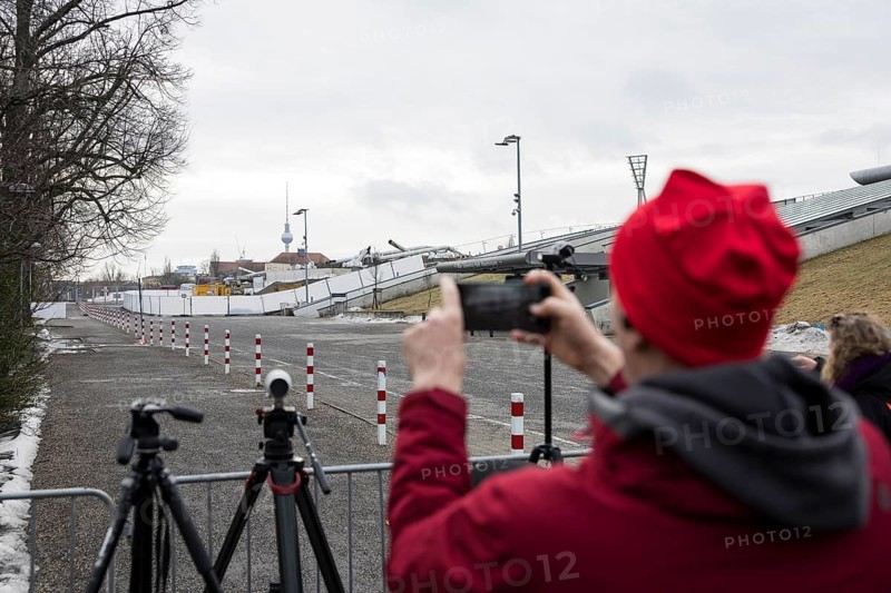 After the controlled demolition of two of the four floodlight towers, a passerby photographs the remains with his cell phone in the Friedrich-Ludwig-Jahn-Sportpark in Berlin on 12.02.2026. The blast is intended to create space for a conversion into a public inclusion park