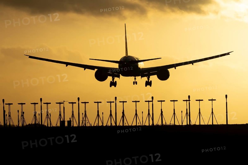 Boeing 777 commercial passenger jet aircraft in flight on approach to land over runway lights silhouette at sunset at London Stansted airport, Essex, England, United Kingdom