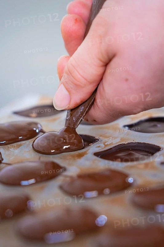 Close-up of a hand filling chocolate molds with chocolate, vegan chocolates production, Haselstaller Hof, Gechingen, Germany