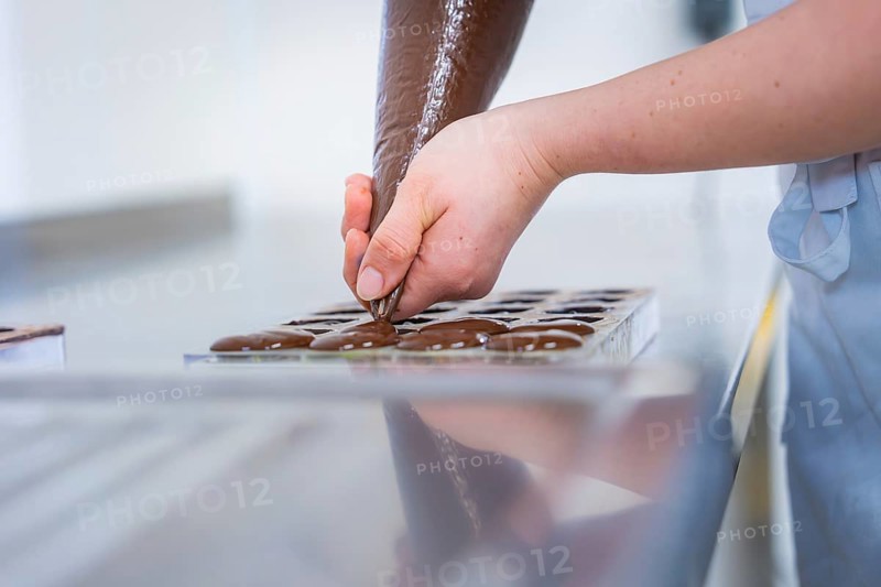 Chocolate is pressed into a chocolate mold by one hand, vegan chocolates production, Haselstaller Hof, Gechingen, Germany