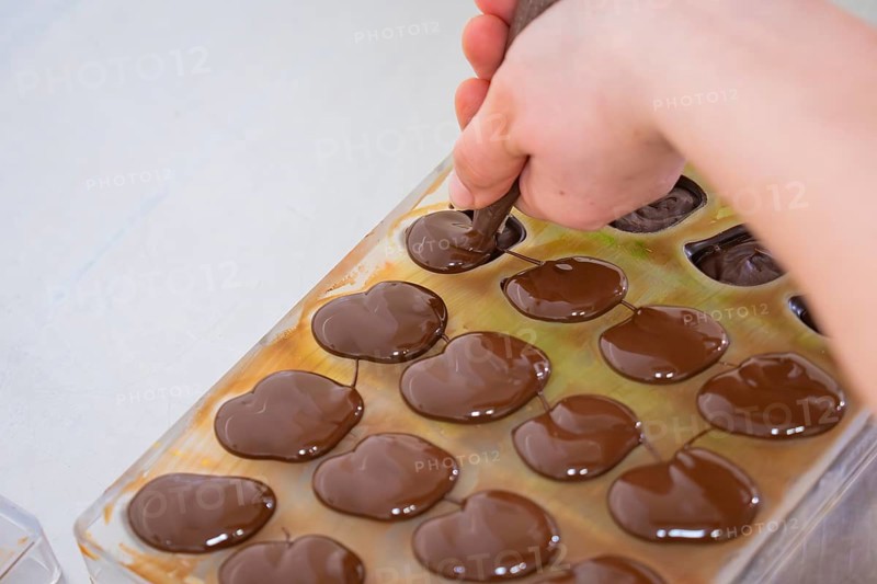 Hand with piping bag fills liquid chocolate in chocolate shape on a table, vegan chocolates production, Haselstaller Hof, Gechingen, Germany