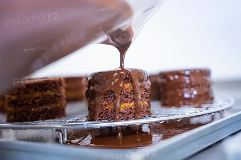 Liquid chocolate is poured over a cake on a grid in a kitchen, Vegan Tart Production, Haselstaller Hof, Gechingen, Germany
