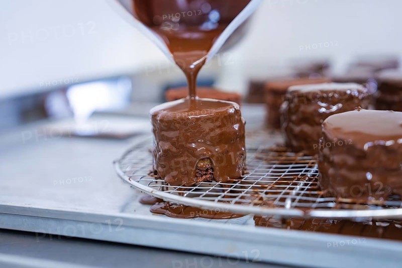 A pastry covered with liquid chocolate drips on a grid in a baking quality kitchen, vegan cake production, Haselstaller Hof, Gechingen, Germany