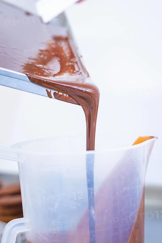 Liquid chocolate is poured from a rectangular container into a plastic container, Vegan Tart Production, Haselstaller Hof, Gechingen, Germany