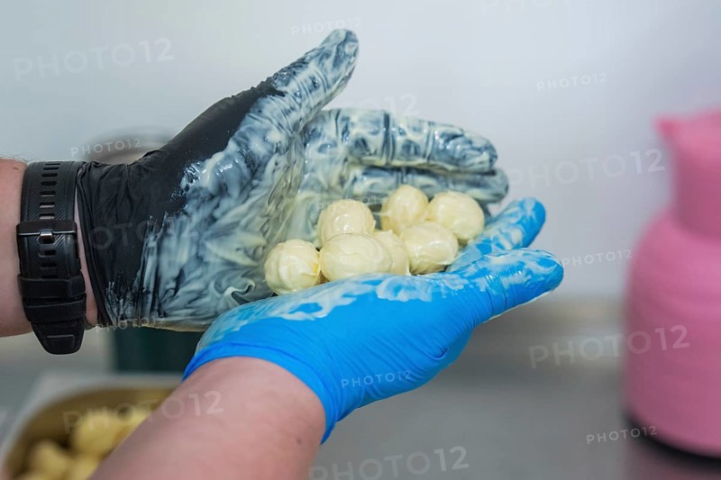A hand in gloves holds chocolates over a bowl with pink and blue decoration, chocolate quail eggs, Easter production, Haselstaller Hof, Gechingen, Germany