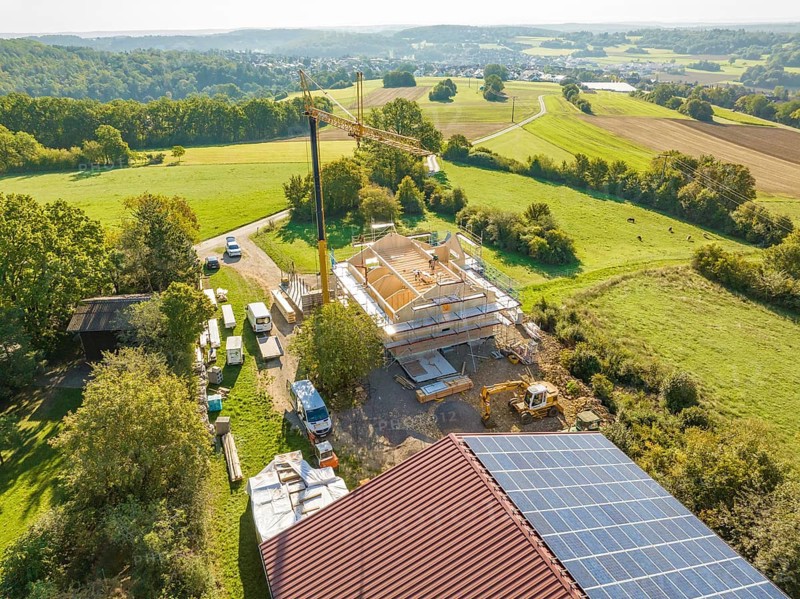 View of construction site with crane and solar panels, surrounded by green countryside and roads, timber house construction, Gechingen, Germany