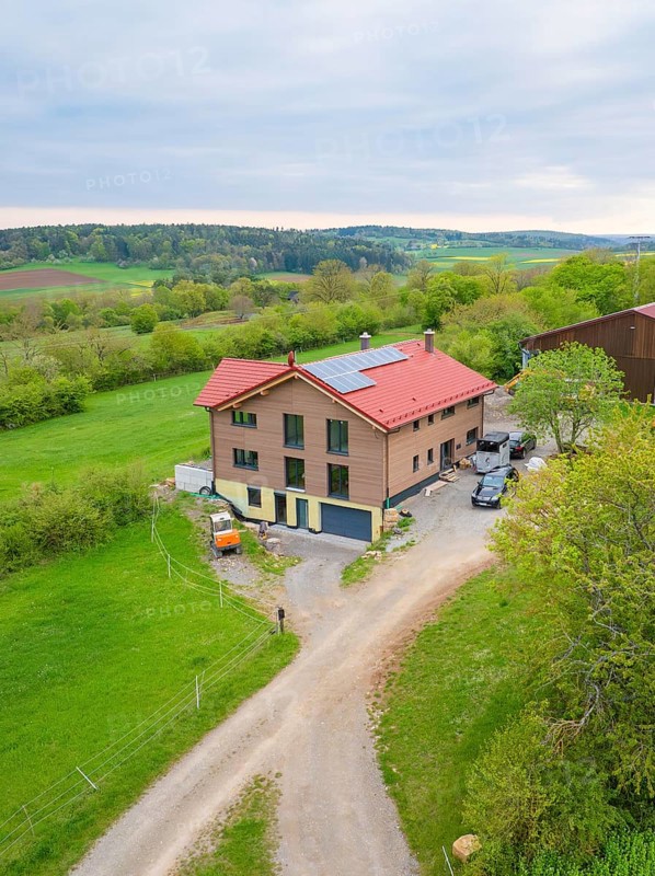 House with red roof and solar panel in rural area with green pastures and a road, Holzhausbau, Gechingen, Germany