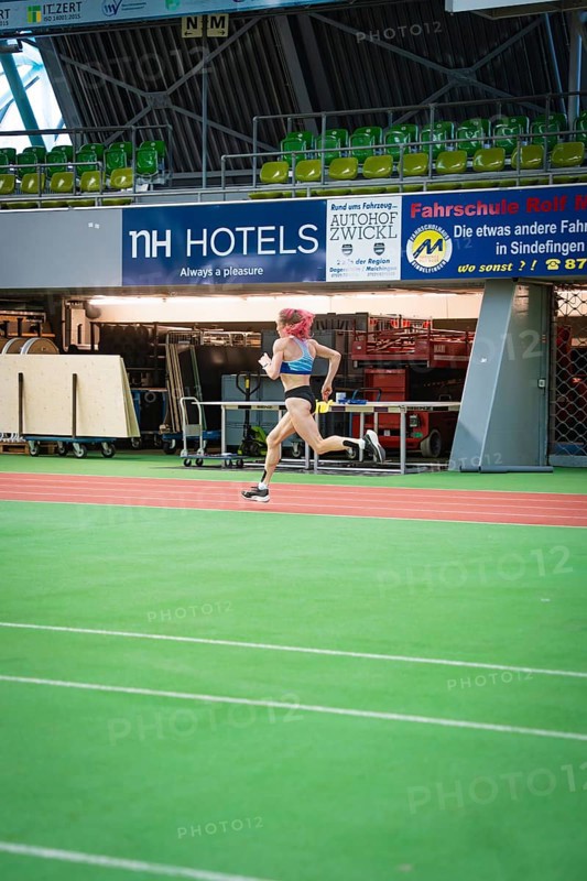 A sporty woman runs at high speed across the green track of a stadium with advertising, middle distance runner Katharina Jaiser, Sindelfingen Glass Palace, Germany