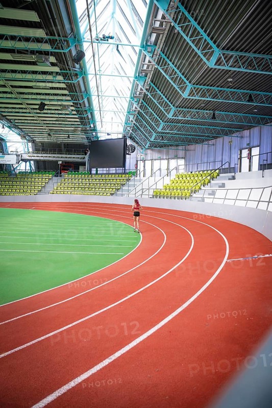 A person runs on an oval, red-green running track of a spacious indoor sports hall, middle distance runner Katharina Jaiser, Glaspalast Sindelfingen, Germany