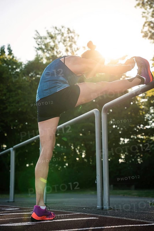 Woman stretches leg over railings surrounded by trees and sunlight, middle distance runner Katharina Jaiser, Gechingen, Germany