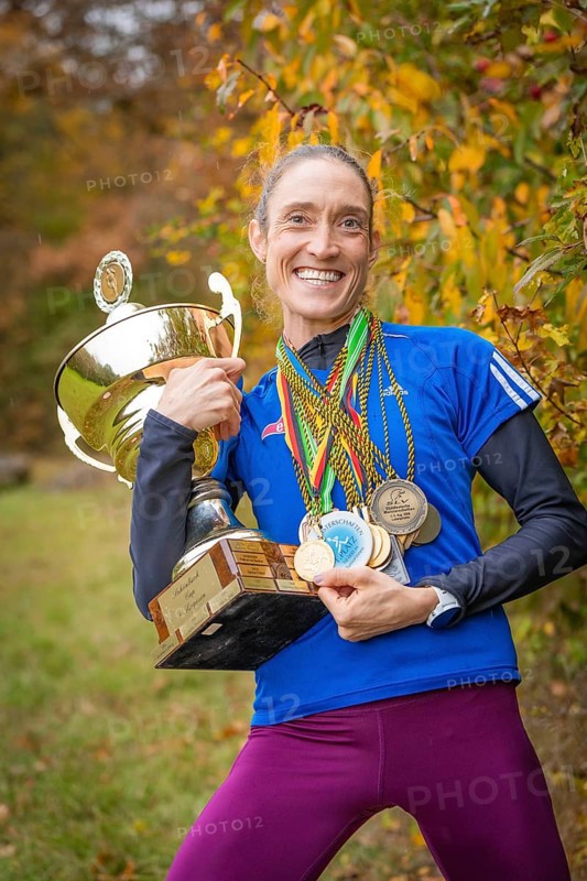 Radiant woman holding a big trophy and many medals in an autumn atmosphere, middle distance runner Katharina Jaiser, Gechingen, Germany