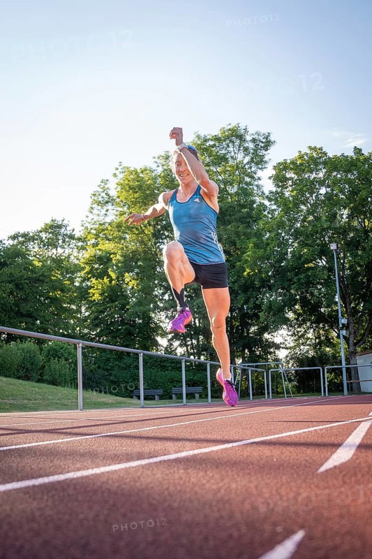Athlete jumping on a track surrounded by green trees and bright sunshine, middle distance runner Katharina Jaiser, Gechingen, Germany