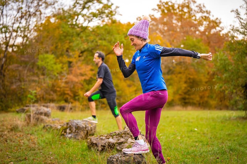 Two people jump off rocks during sporting activity in autumn forest, middle distance runner Katharina Jaiser, Gechingen, Germany
