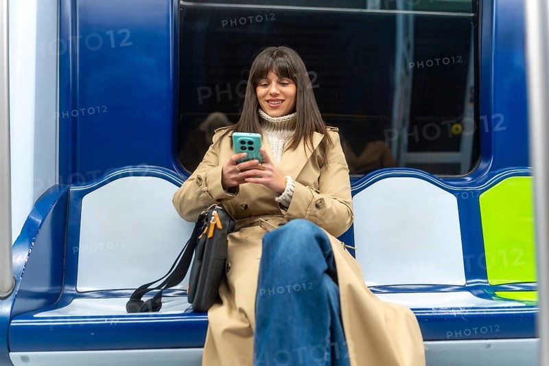 Young woman sitting on a subway train, actively engaging with her smartphone during a daily commute, representing an urban lifestyle and digital connectivity on public transportation