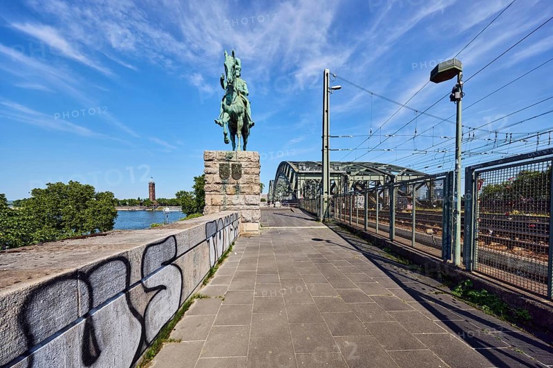 Equestrian statue of Emperor Frederick III, Hohenzollern Bridge, arched bridge, steel arches, metal fence, sandstone wall, catenary masts, overhead lines, lantern, graffiti, footpath made of paving slabs, trees, blue sky, cirrus clouds, Cologne, district-free city, North Rhine-Westphalia, Germany