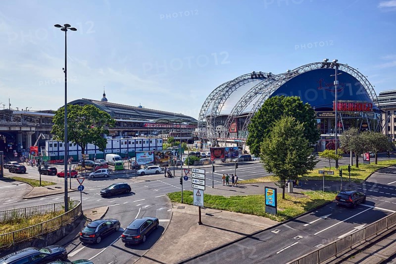 Large tent Musical Dome, general architecture, lantern, main station, roads, lanes, central island, pedestrian crossing, vehicles, parking lot, lawn, trees, elevated perspective, side light, blue sky, cloudless, federal road B51, Konrad-Adenauer-Ufer intersection with Trankgasse, Cologne, district-free city, North Rhine-Westphalia, Germany
