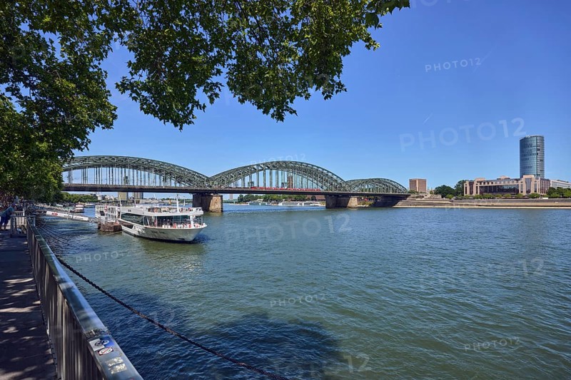 Rhine river, Hohenzollern bridge, pedestrian and railway bridge, arched bridge, steel arches, MaxCologne high-rise building, pier, gangway, wharf, metal railing, water surface with small waves, branches, trees, blue sky, cloudless, Leystapelwerft, Cologne, district-free city, North Rhine-Westphalia, Germany