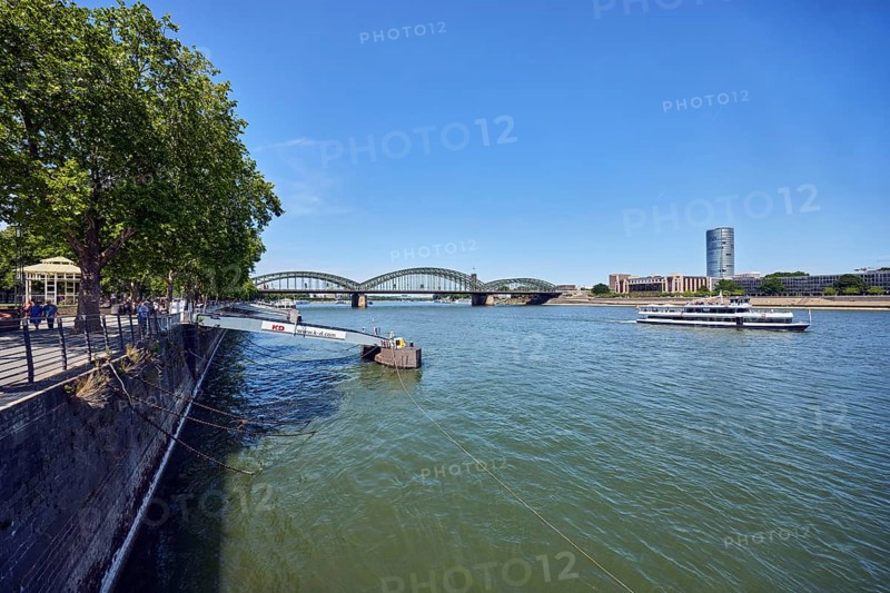 Rhine river, sightseeing boats, total view, general architecture, high-rise buildings, pedestrian and railway bridge Hohenzollern Bridge, arched bridge, steel arches, pier, gangway, quay wall, waterfront, trees, blue sky, cloudless, Leystapelwerft, Cologne, district-free city, North Rhine-Westphalia, Germany